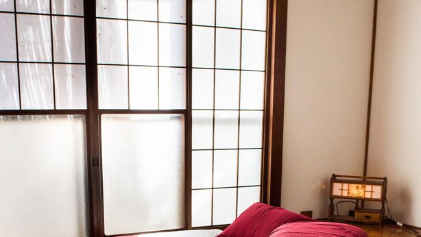 Une pièce avec un sol recouvert de tatamis, un futon servant de lit, une petite table avec des serviettes et une lampe traditionnelle japonaise.