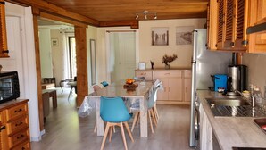 A modern kitchen with wooden cabinets, a stainless steel refrigerator, and a dining area with a table and chairs.