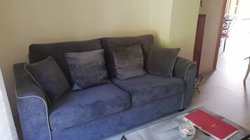 A grey sofa with patterned cushions in a room with a tiled floor and a small table with a red book and a glass object.