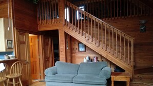 Un salon chaleureux avec un escalier en bois, un canapé gris et un tapis coloré.
