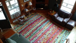 Un salon chaleureux avec un tapis rayé aux couleurs vives, un canapé en cuir, une table basse en bois, un téléviseur et une cheminée.