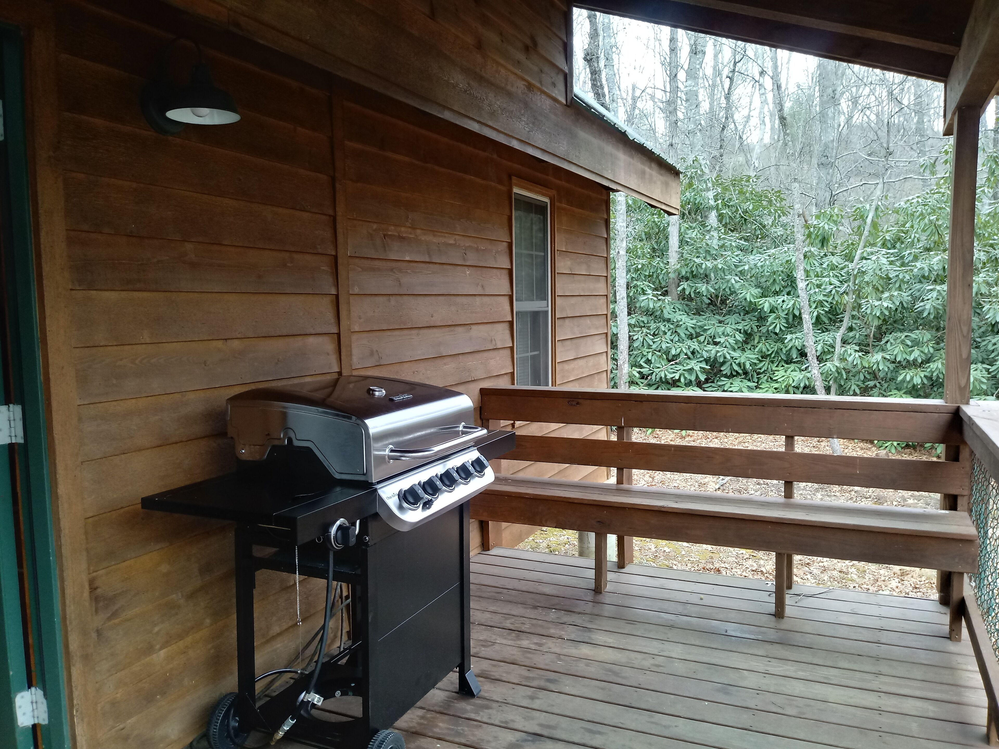 Una terraza de madera con una parrilla y un banco.