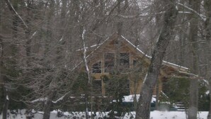 Une cabane entourée d’arbres, et la neige recouvre le sol.