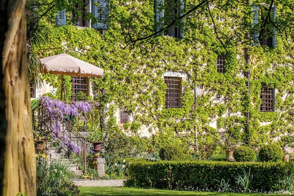 Un bâtiment aux murs recouverts de lierre, un jardin agrémenté d’une haie et une pergola surmontée d’une tonnelle.