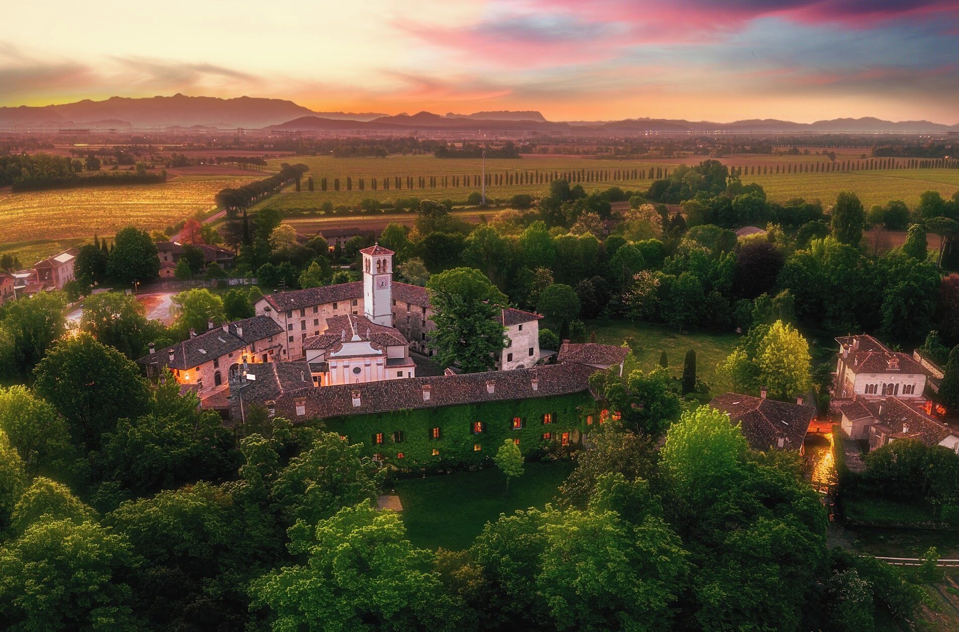 Vue aérienne d’une ville historique, dominée par une église remarquable avec un clocher, entourée d’une végétation luxuriante et de vignobles.