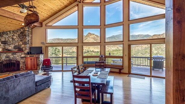 A spacious living room with a stone fireplace, large windows, and a balcony overlooking a mountainous landscape.