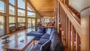 A spacious living area with a wooden ceiling, large windows, a wooden staircase, and a cozy seating area.