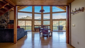 A spacious living area with a large window overlooking mountains, wooden flooring, and a stone fireplace.