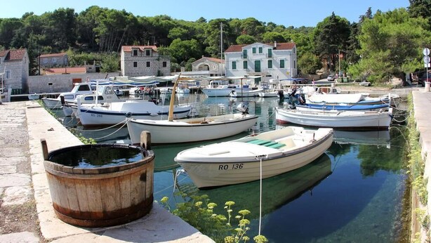 Uma marina com barcos atracados, um barril de madeira e edifícios ao fundo.