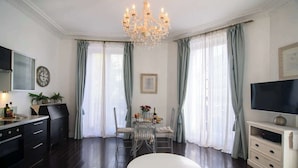 A modern living room with a dining area, a chandelier, a television, and a clock on the wall. - Perfectly Parisian, Bright & Elegant with Balcony (Paris)