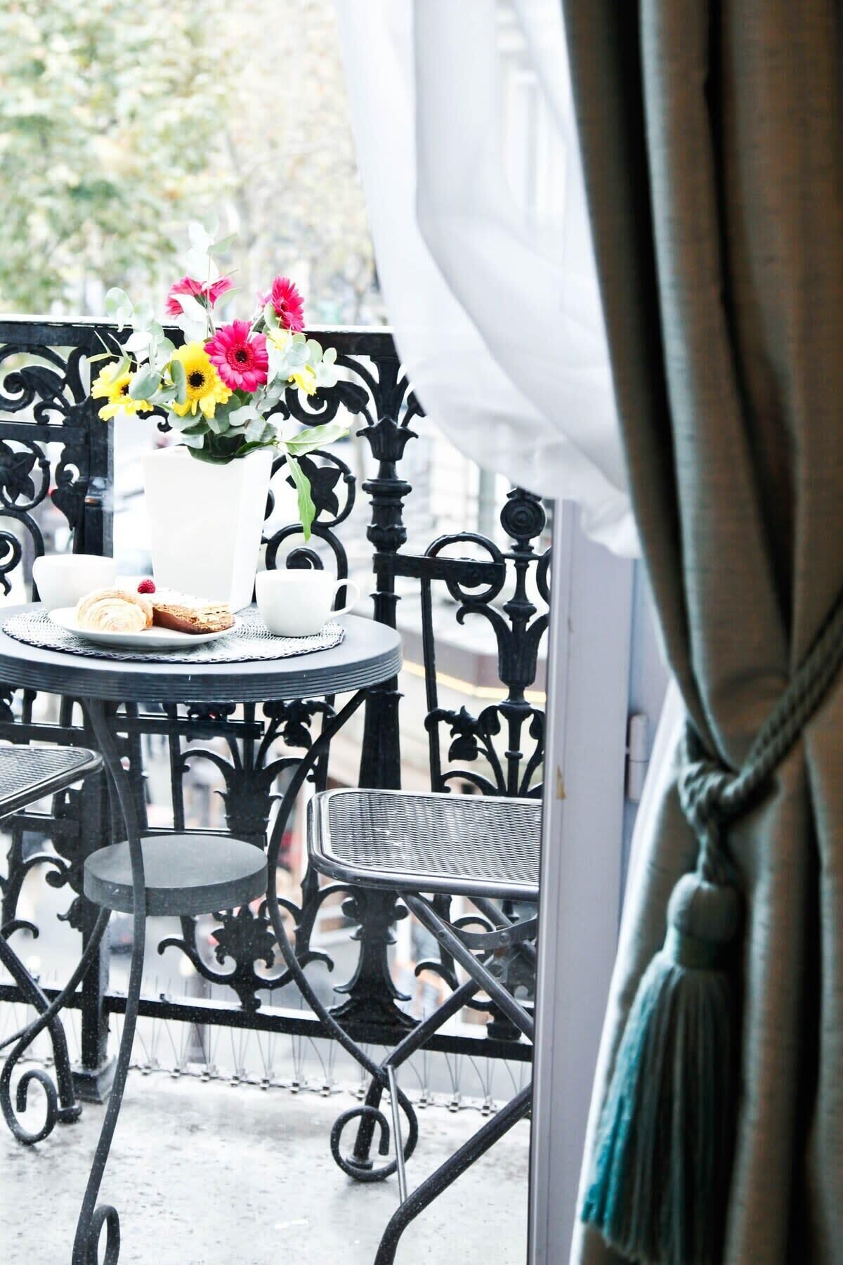 A balcony with a round table, a white vase with flowers, and a plate with pastries.