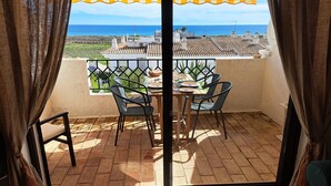 A balcony with a table and chairs, a view of the sea, and a yellow-striped awning.