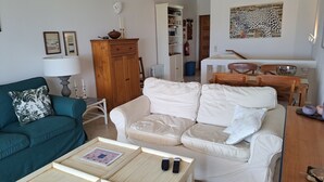 A living room with a teal sofa, a white sofa, and a wooden coffee table with books and remotes.