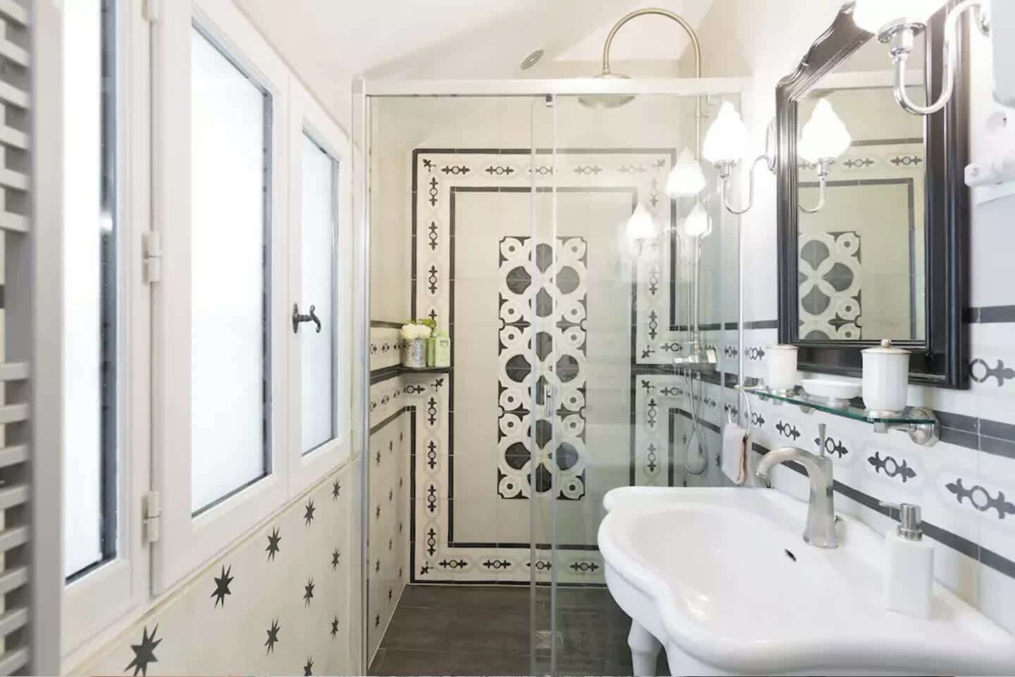 Un bagno con cabina doccia in vetro, un lavandino bianco e uno specchio con cornice nera.
