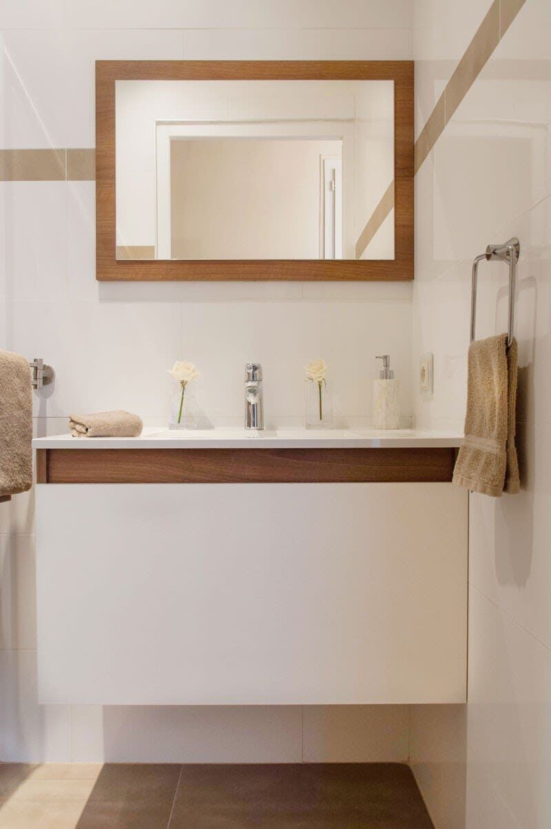 A modern bathroom with a white vanity, a wooden-framed mirror, and a towel rack.