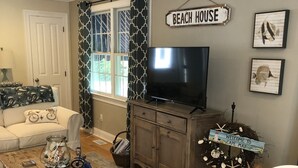 A living room with a television, a coffee table, a sofa, and a sign that reads "BEACH HOUSE". - Cape May Beautiful Condo(5minutes to the Beach) (Cape May)