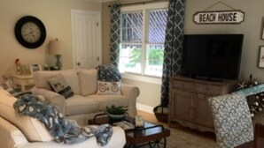 A living room with a white sofa, a television, a ceiling fan, and a sign that reads "BEACH HOUSE". - Cape May Beautiful Condo(5minutes to the Beach) (Cape May)