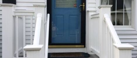 A front view of a house with a blue door, white railings, and a small porch.