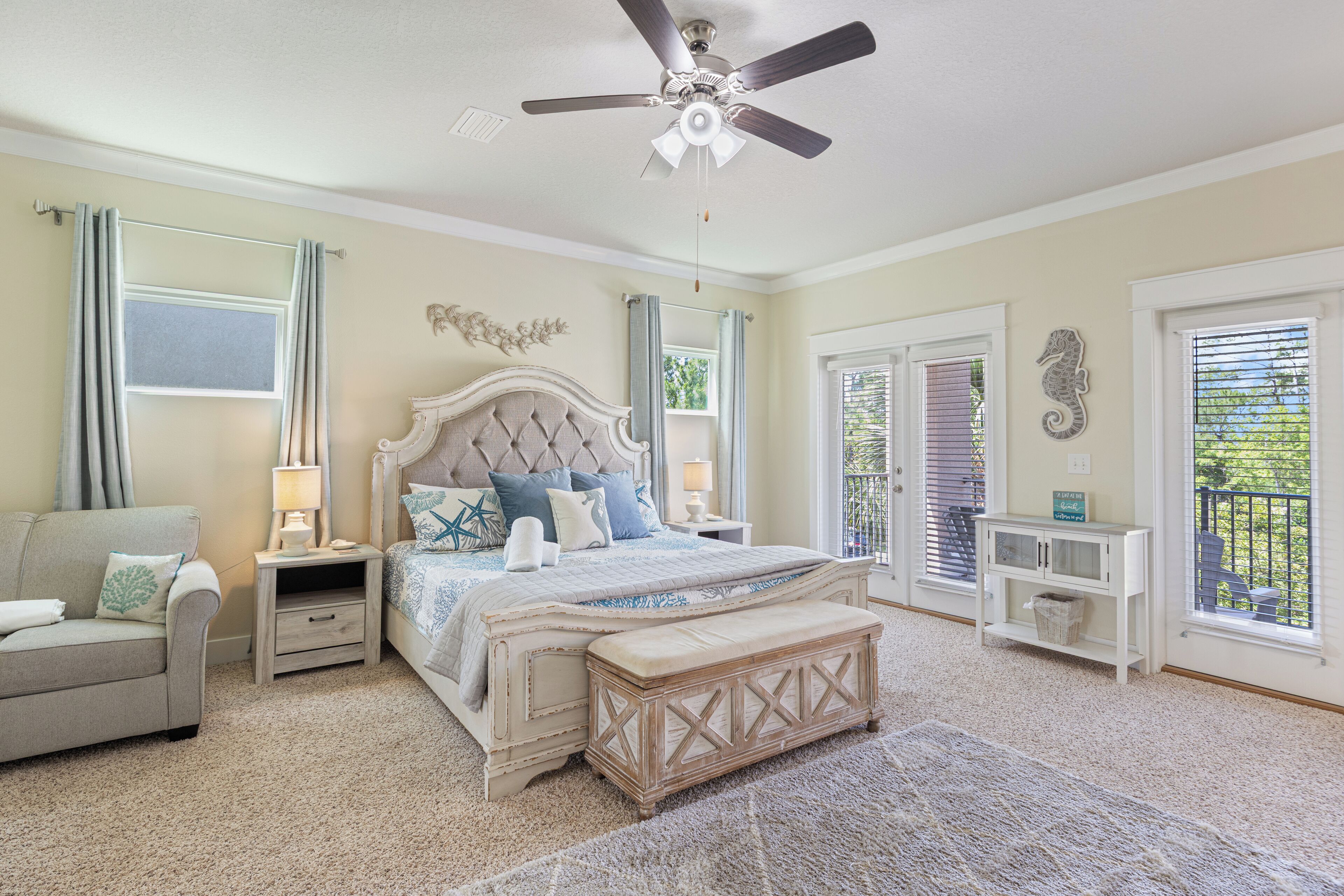 A bedroom with a bed, nightstands, a bench, a sofa, a ceiling fan, and a window with blinds.