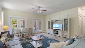 Un salón espacioso con ventilador de techo, mesa de billar y televisor. Dos puertas dan acceso a un patio.