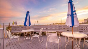 En terrasse med udendørs møbler, inklusive borde og stole, samt to parasoller.