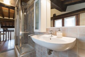 Un baño con cabina de ducha de vidrio, un lavabo blanco con dispensador de jabón y paredes de azulejos.