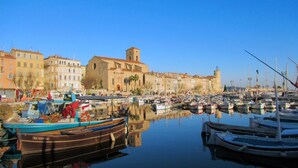 Una marina con barche ormeggiate, un edificio storico con una torre e un cielo azzurro limpido.