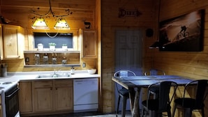 A cozy cabin-style kitchen with wooden cabinets, a sink, a stove, and a dining area with a table and chairs.