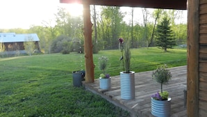 A wooden deck with potted plants, a metal spiral sculpture, and a view of a grassy yard and trees.
