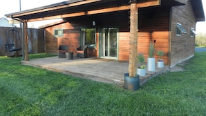 A modern wooden house with a covered patio, sliding glass doors, and outdoor seating.