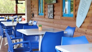 Une cabane en bois avec des chaises et des tables bleues, un panneau représentant une planche de surf et un téléviseur accroché au mur.