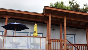 Une terrasse en bois avec une rambarde en verre, un parasol jaune et un parasol bleu.