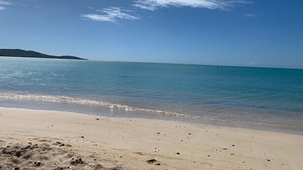 Une plage avec une eau d’un bleu limpide et un rivage sablonneux.