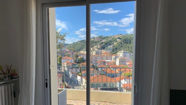 Quarto com vista para uma varanda com azulejos e para a paisagem urbana.