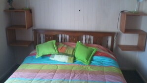 Una cama con un colcha colorida, dos almohadas verdes y cabecera de madera.