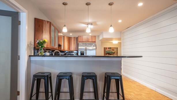 A modern kitchen with wooden cabinets, a stainless steel refrigerator, and a bar area with stools. - Location! 1 Block from Bayshore / SOHO / Hyde Park (Tampa)