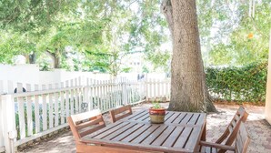 An outdoor patio with a wooden table and chairs, surrounded by a white picket fence, under a large tree. - Location! 1 Block from Bayshore / SOHO / Hyde Park (Tampa)
