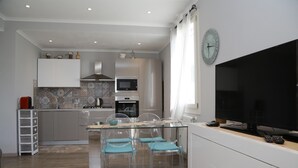 Ett modernt kök med en matplats, med ett bord med glasskiva, genomskinliga stolar och en stor TV med platt skärm.