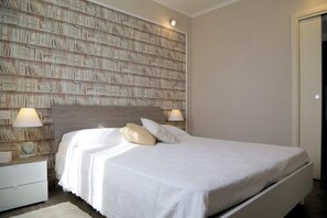 A neatly arranged bedroom with a large bed, two bedside tables, a bookshelf, and a door.