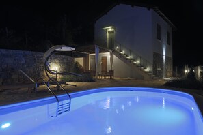 Una piscina con un muro de piedra y una escalera que lleva a una casa.