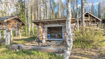 Tunnelmallinen, maalaishenkinen mökki, jossa on puinen terassi ja nuotiopaikka, ja sen ympärillä on metsää.