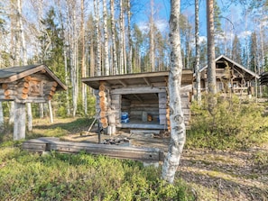 A rustic cabin with a wooden deck and a fire pit, surrounded by a forest.