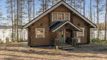 Une petite cabane en bois avec un toit à pignon, une véranda à l’avant et une cheminée bien visible.