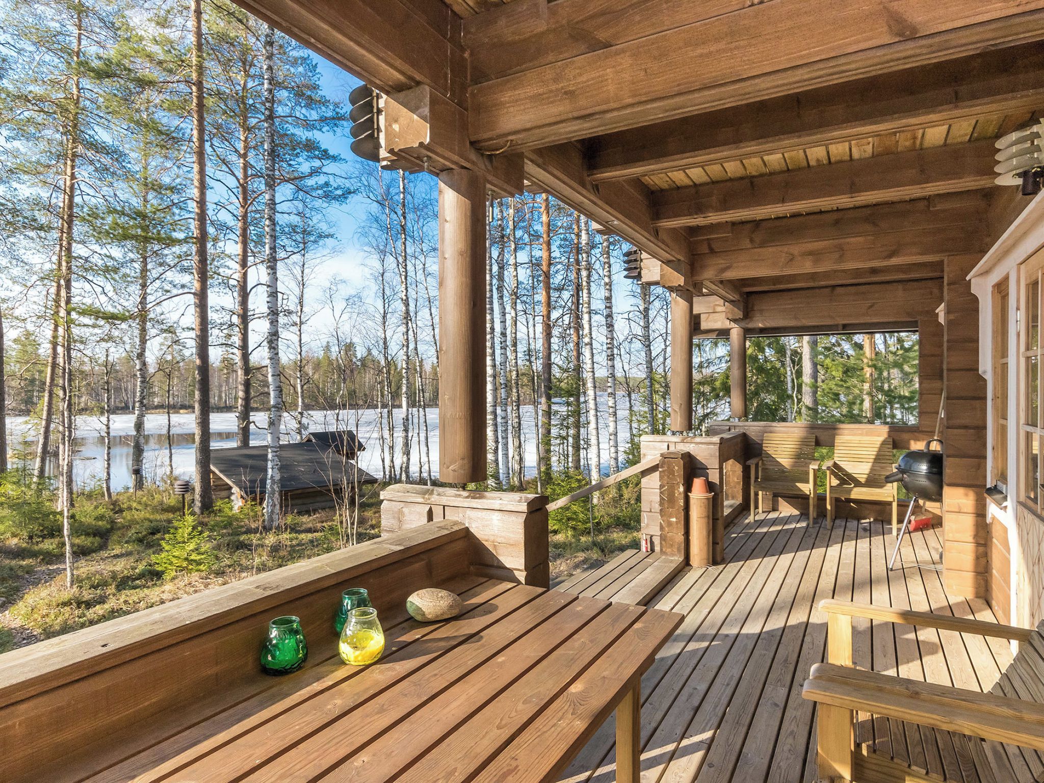 A wooden deck with outdoor seating and a view of a forest and lake.