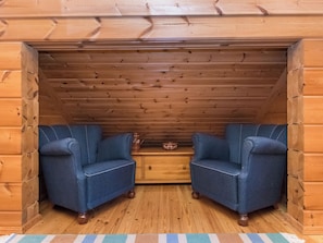 Het interieur van een blokhut met twee gestoffeerde fauteuils, een houten kist en een houten vloer.