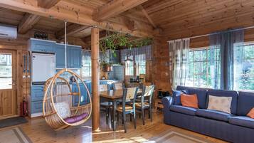 A wooden cabin interior with a dining area, a hanging chair, a sofa, and a kitchen.