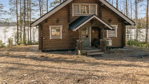 A wooden cabin with a front porch, a small staircase, and a view of a forested area.