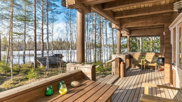 A wooden deck with a view of a lake and trees, outdoor seating, and a grill.