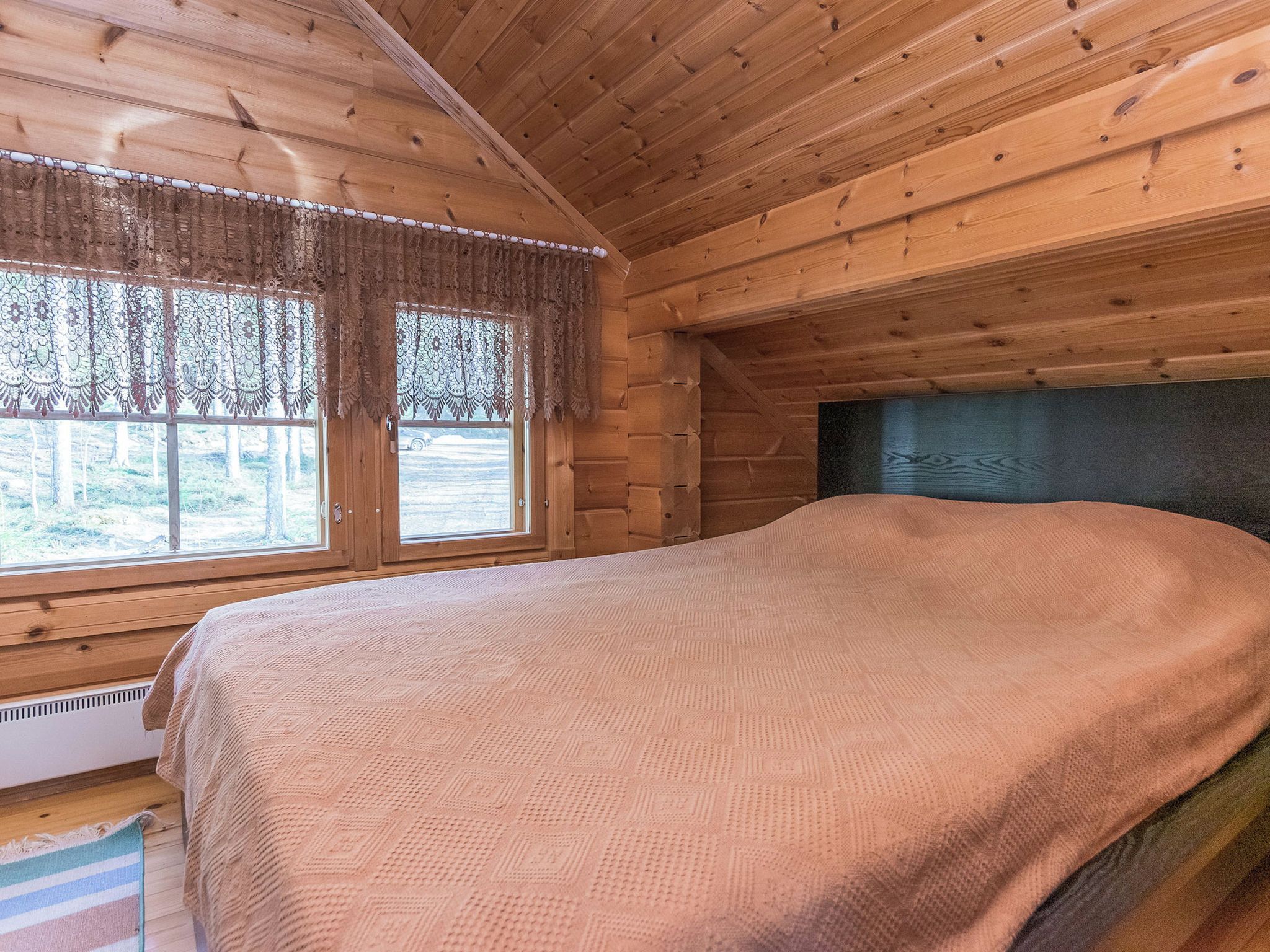 Een houten kamer met een bed, ramen en uitzicht op de omgeving.