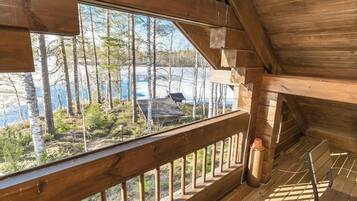 Une cabane en bois dotée d’un balcon donnant sur une zone boisée et un lac.